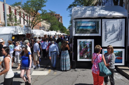A bustling street fair with art displays, tents, and crowds of people enjoying the vibrant atmosphere.