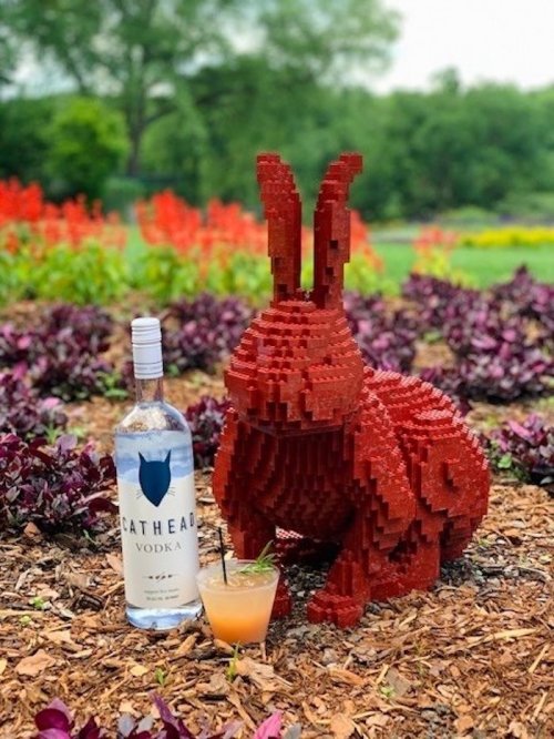A red LEGO rabbit sits in a garden, next to a bottle of Cathead Vodka and a cocktail.