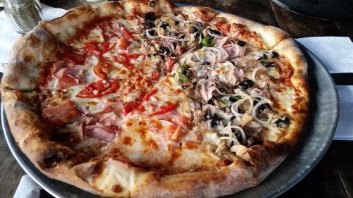 A large pizza divided into two halves, one topped with ham, peppers, and cheese, the other with olives, onions, and chicken.