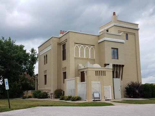A large, beige building with decorative architectural features and a cloudy sky in the background.