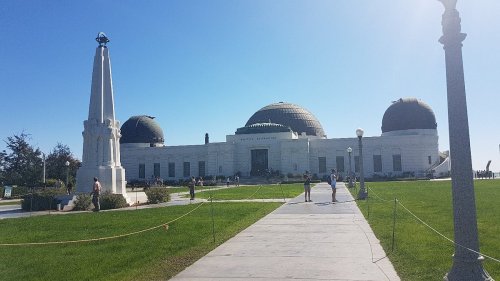 Griffith Observatory with domes, surrounded by green grass and visitors under a clear blue sky.