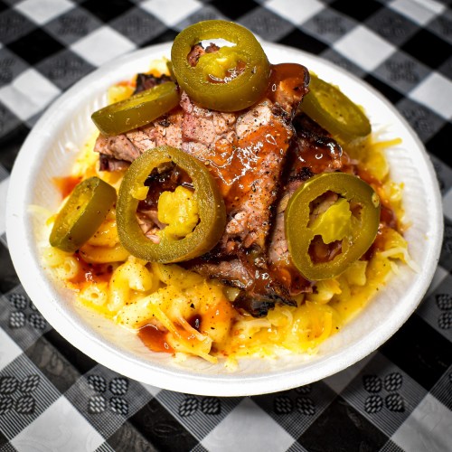A plate of barbecue meat topped with jalapeños and sauce, served over a bed of creamy coleslaw on a checkered tablecloth.