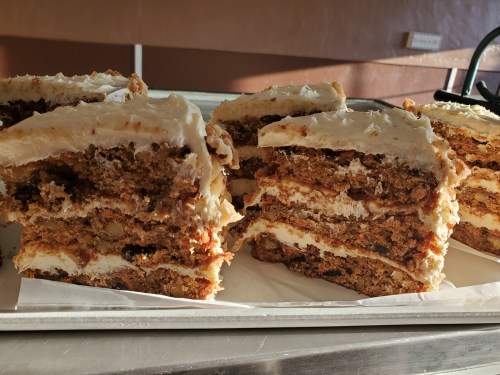 Slices of layered cake with cream frosting, showcasing rich textures and a mix of nuts and fruits.