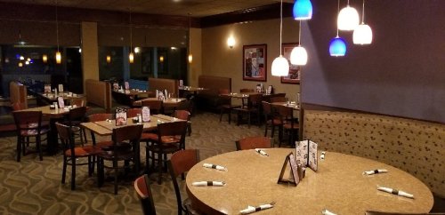 A spacious restaurant interior with tables set for dining, featuring soft lighting and a cozy atmosphere.