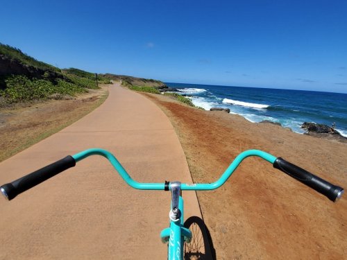 View from a bike handlebars on a coastal path, with ocean waves and blue sky in the background.
