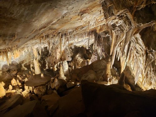 A dimly lit cave interior featuring various stalactites and stalagmites, with rocky formations and textures.