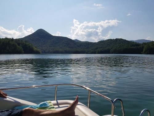 A serene lake view with mountains in the background and a clear blue sky, seen from a boat.
