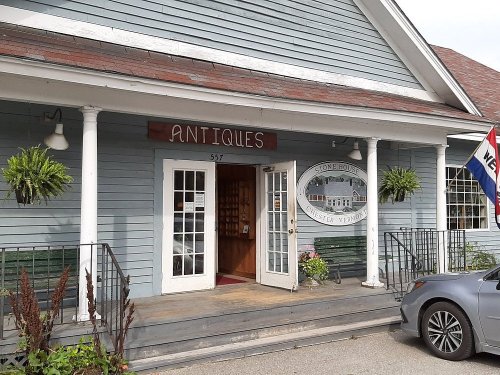 A charming antique shop with a blue exterior, welcoming entrance, and hanging plants, located in Chester, Vermont.