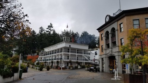 Historic buildings in a quaint town square, surrounded by trees and a cloudy sky.