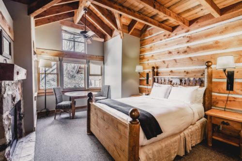 Cozy cabin bedroom with wooden walls, a queen bed, a table, and large windows letting in natural light.