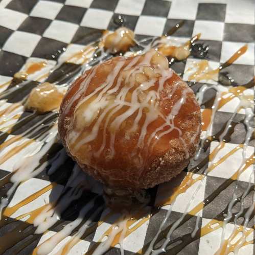 A round dessert drizzled with caramel and white icing, placed on a black and white checkered paper.