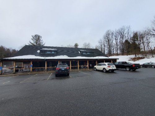 A parking lot with several cars in front of a large, snow-dusted building under a cloudy sky.