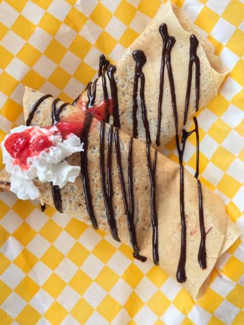 Two crepes drizzled with chocolate sauce, topped with whipped cream and a cherry, on a yellow checkered paper.