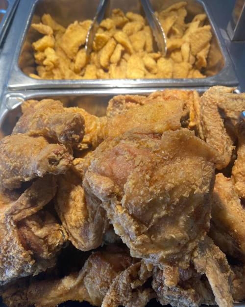 A close-up of a tray filled with crispy fried chicken pieces, with more wings in the background.