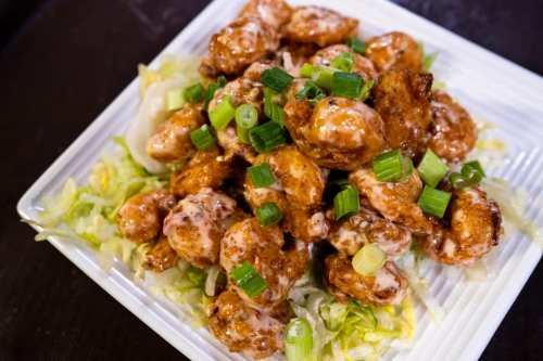A plate of crispy shrimp coated in a sweet sauce, garnished with green onions, served on a bed of lettuce.