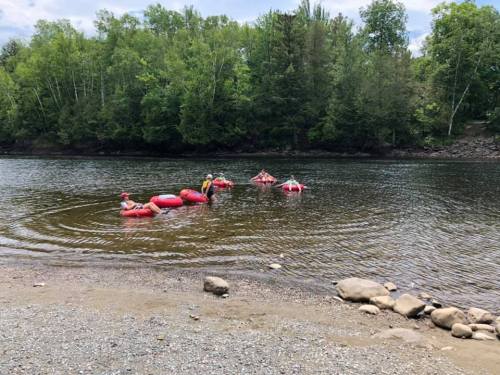 People floating on red inner tubes in a calm river, surrounded by trees and rocky shore.