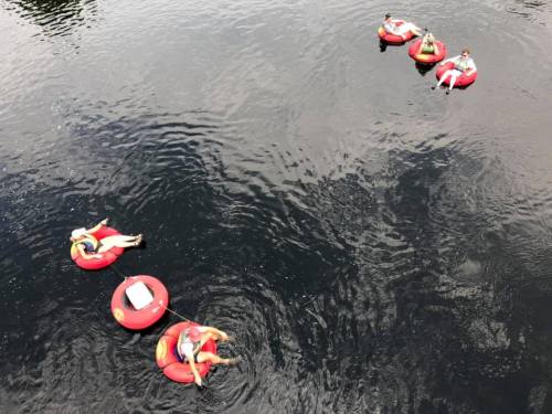 Aerial view of people relaxing on red inner tubes in a dark water body, enjoying a sunny day.