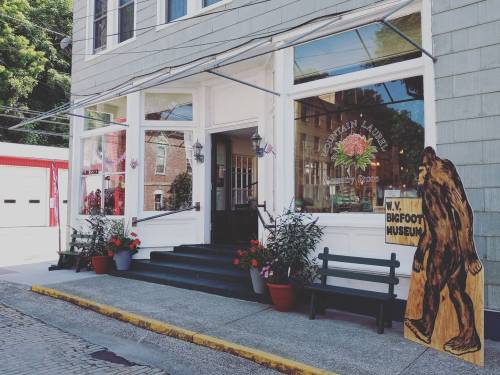 A storefront with a sign for a Bigfoot museum and flower planters, featuring a wooden Bigfoot cutout outside.