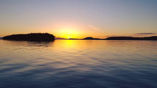 Sunset over calm waters, with silhouettes of islands against a colorful sky.