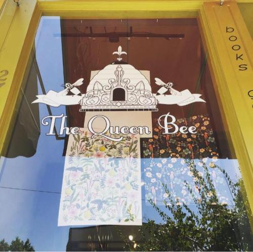 Sign for "The Queen Bee" shop featuring a bee design and floral patterns in the window. Bright yellow exterior.