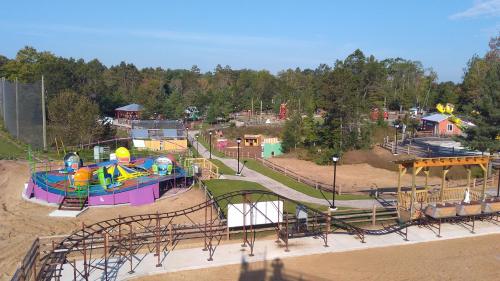 Aerial view of a colorful amusement park with rides, pathways, and greenery under a clear blue sky.