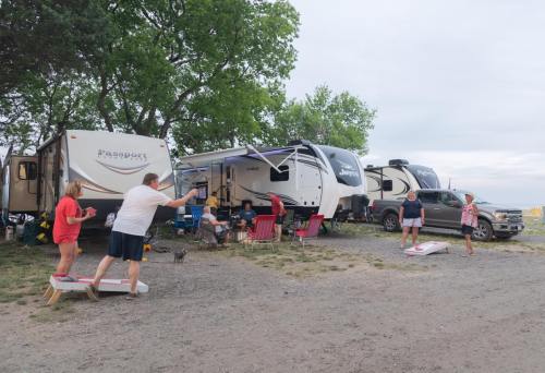 A group of people enjoying a camping trip, playing cornhole near RVs and a truck under a cloudy sky.