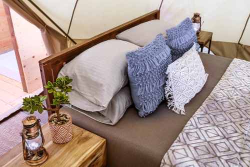 Cozy tent interior with a bed featuring decorative pillows, a plant, and lanterns on wooden nightstands.