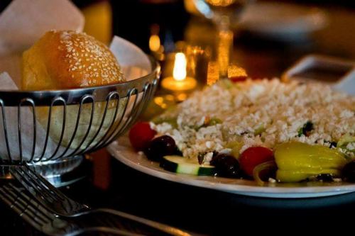A plate of salad with vegetables and feta cheese beside a sesame seed bun in a basket, with soft candlelight in the background.