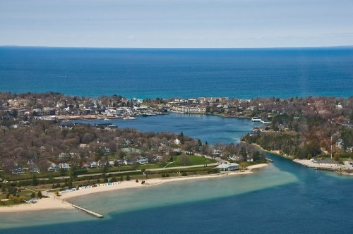 Aerial view of a coastal town with sandy beaches, green parks, and blue waters under a clear sky.
