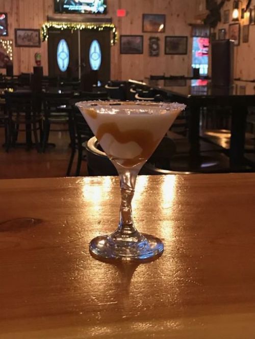 A cocktail in a glass with a salted rim, sitting on a wooden bar in a dimly lit pub.