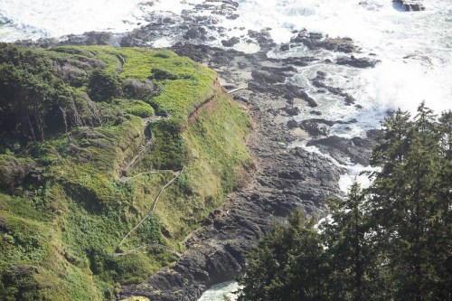 A coastal landscape featuring rocky cliffs, lush greenery, and waves crashing against the shore.