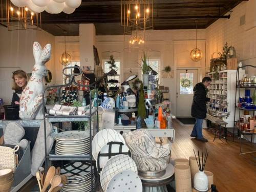 A cozy shop filled with home decor items, pottery, and a woman browsing among the displays.