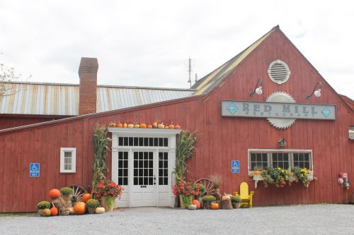 A red barn-style restaurant with pumpkins and flowers decorating the entrance, set against a cloudy sky.