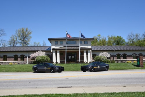 Two police cars parked in front of a modern building with flags and trees in a clear blue sky.