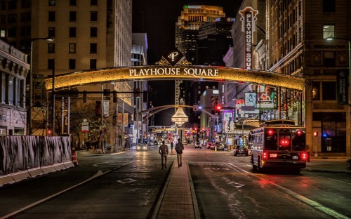 Night view of Playhouse Square, featuring a lit archway and city buildings, with two people walking down the street.