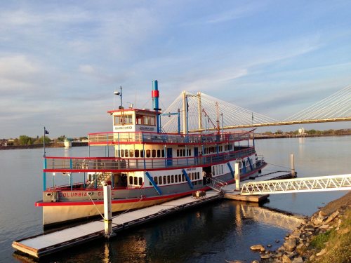 A colorful riverboat named "Columbia" docked by a shore with a bridge in the background under a clear sky.