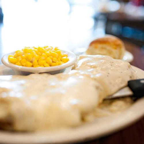 A plate of biscuits smothered in gravy, served with a side of corn and a biscuit.
