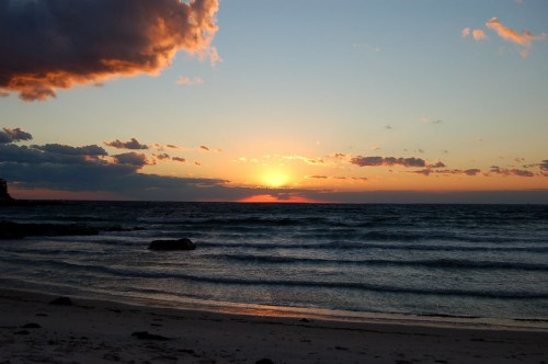 A serene beach at sunset, with vibrant colors in the sky and gentle waves lapping at the shore.