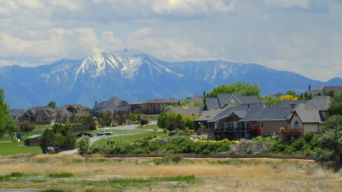 A scenic view of a suburban neighborhood with mountains in the background, featuring snow-capped peaks and greenery.