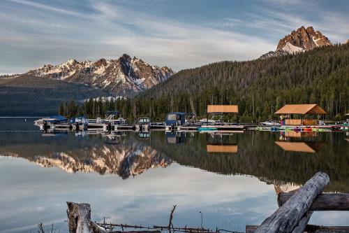 A serene lake scene with mountains, docks, and boats reflecting on calm water under a clear sky.