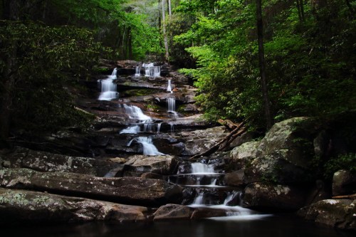 A serene waterfall cascades over rocky steps, surrounded by lush green trees and foliage.