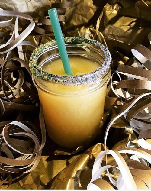 A jar of orange drink with a green straw, surrounded by gold and brown decorative ribbons.