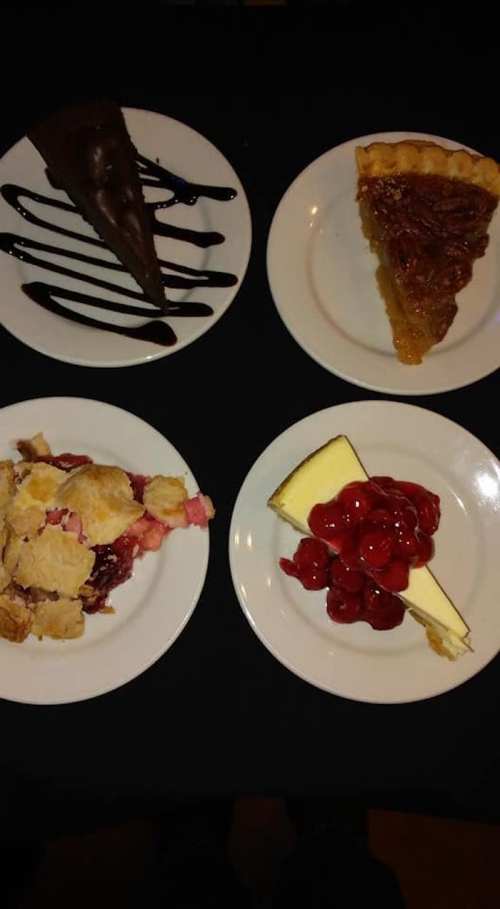 Four dessert plates: a chocolate slice, pecan pie, cherry cheesecake, and fruit cobbler, all on white plates.