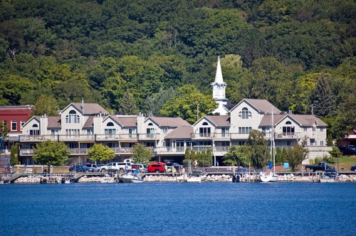 A waterfront view of a charming town with buildings, a church steeple, and boats along the shore.