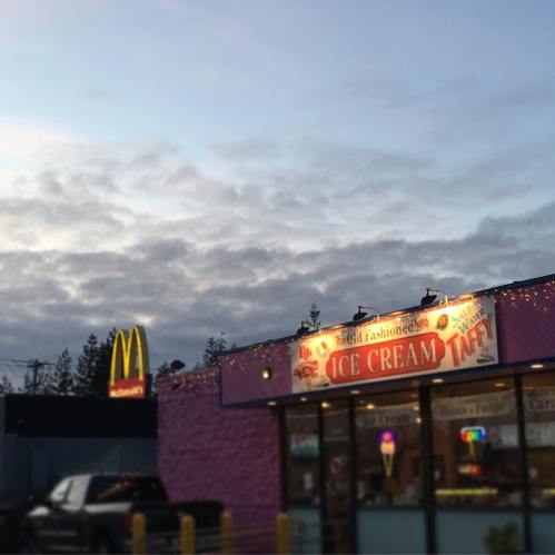 A colorful ice cream shop with a McDonald's sign in the background under a cloudy sky.