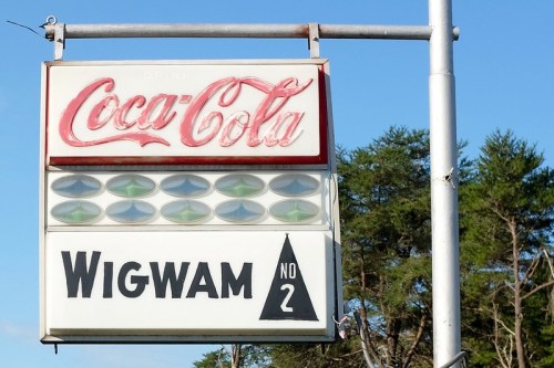 Coca-Cola sign above a "Wigwam No. 2" sign, with green lights and a clear blue sky in the background.