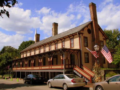 Historic building with a wooden facade, porch, and American flags, set against a blue sky with clouds.