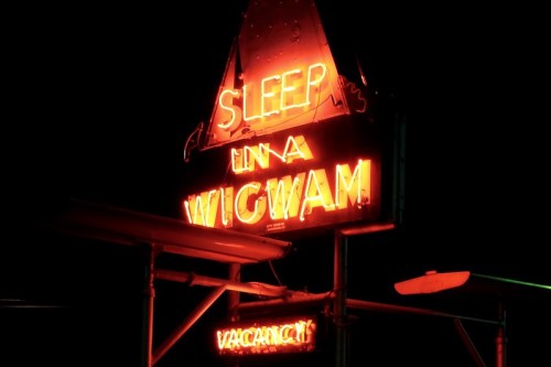 Neon sign reading "SLEEP IN A WIGWAM" illuminated at night, with "VACANCY" below it.