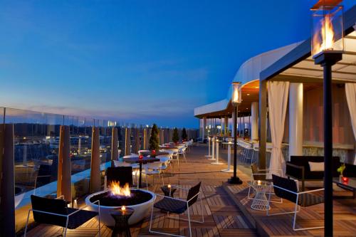 Rooftop terrace at dusk with seating, fire pits, and city views, illuminated by lanterns and soft lighting.