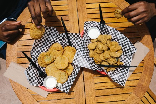 Two baskets of fried food on a wooden table, one with large round pieces and the other with smaller, nugget-shaped pieces.